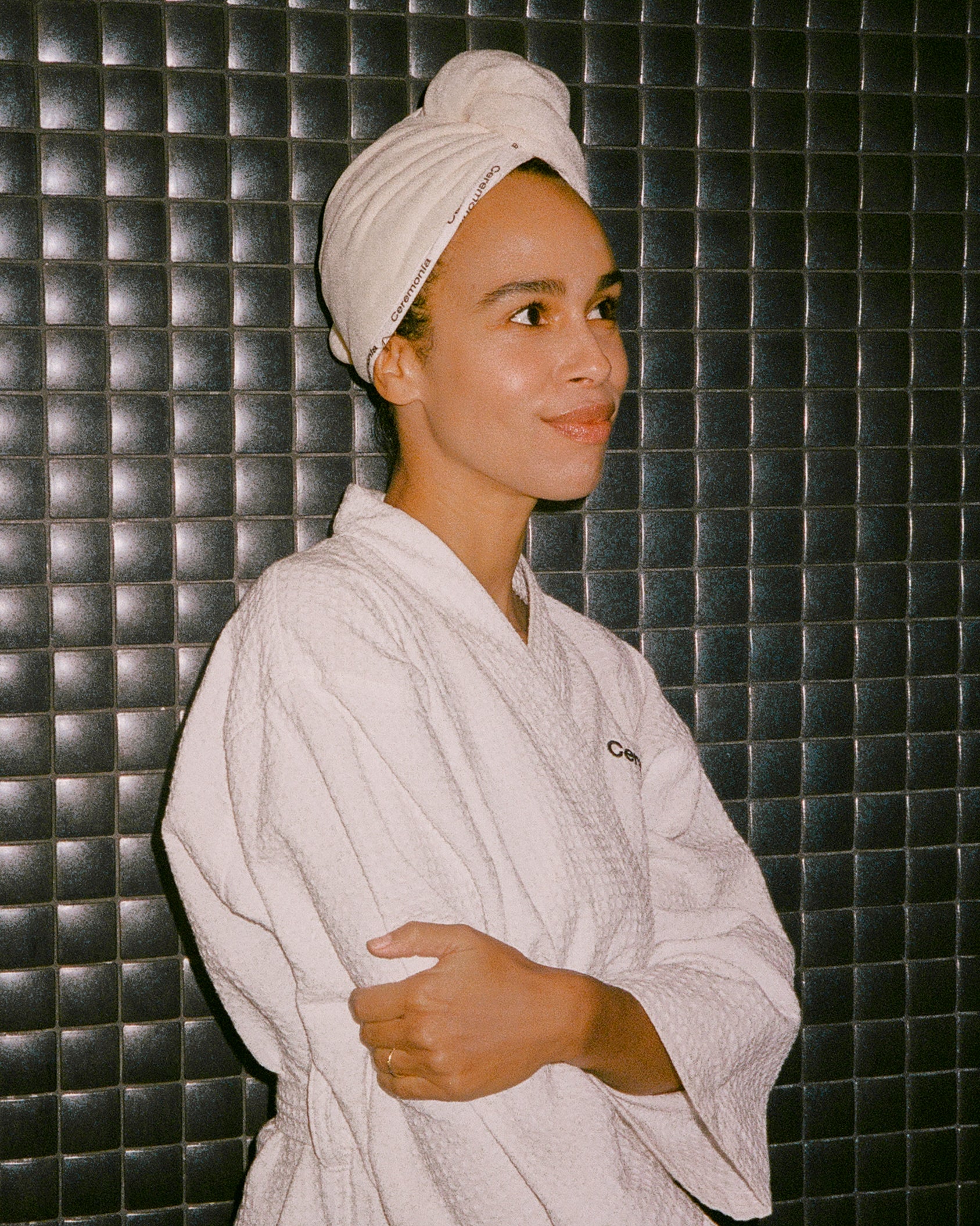 Hair towel wrapped around head with Ceremonia branding, worn with a matching white robe against a tiled wall background.