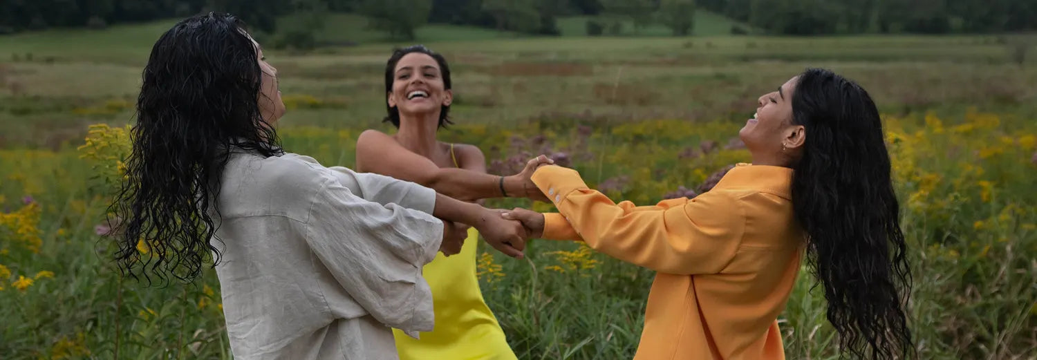 Three women laughing together in a meadow, hair down and freshly washed