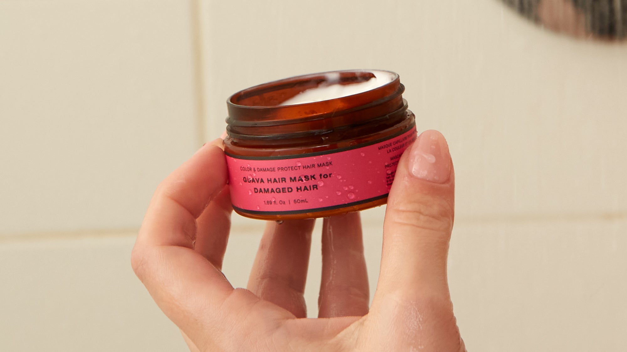 Hand holding an open travel-size Guava hair mask for damaged hair, 50mL jar.
