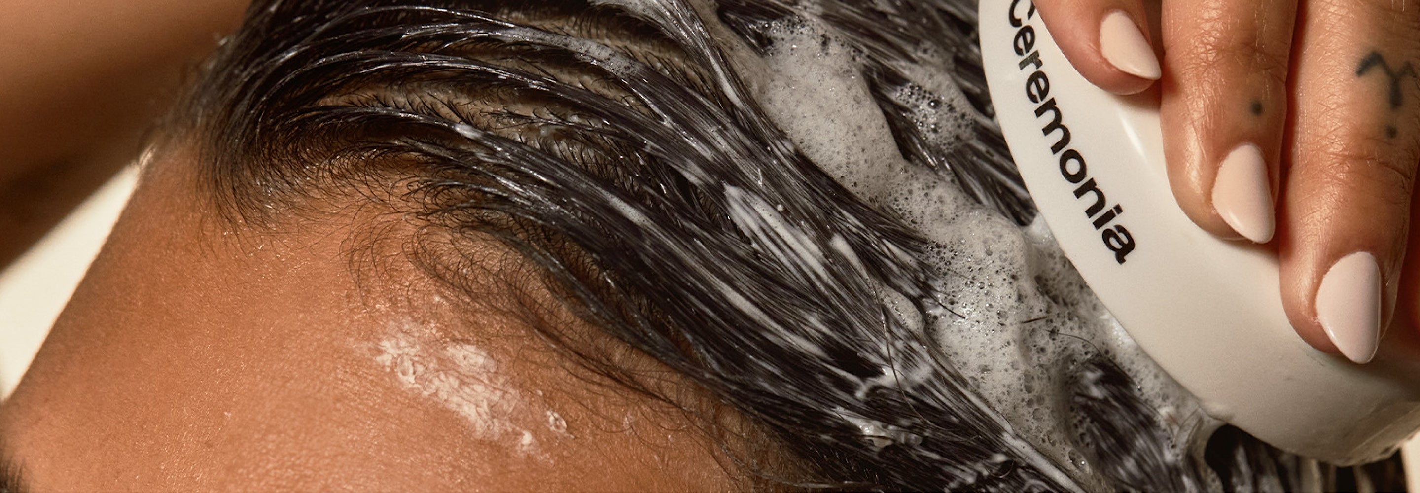 Close-up of lathered wet hair being washed with a Ceremonia scalp brush.