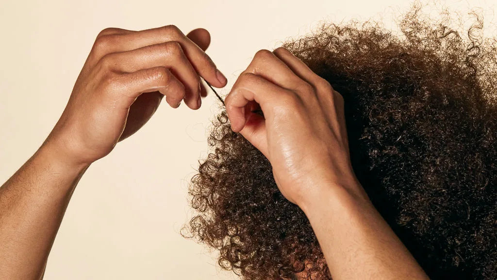 Fingers applying curl defining gel to shape a section of dark textured coils.