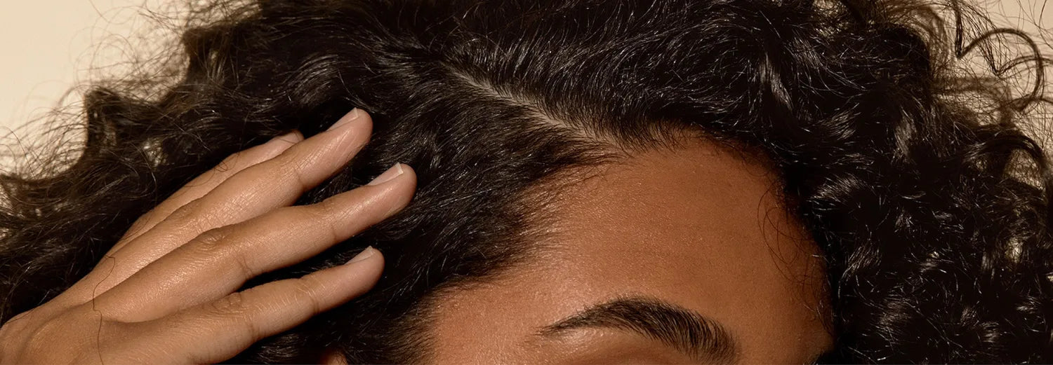 Fingers running through curly dark hair at the roots, close-up on a healthy scalp.