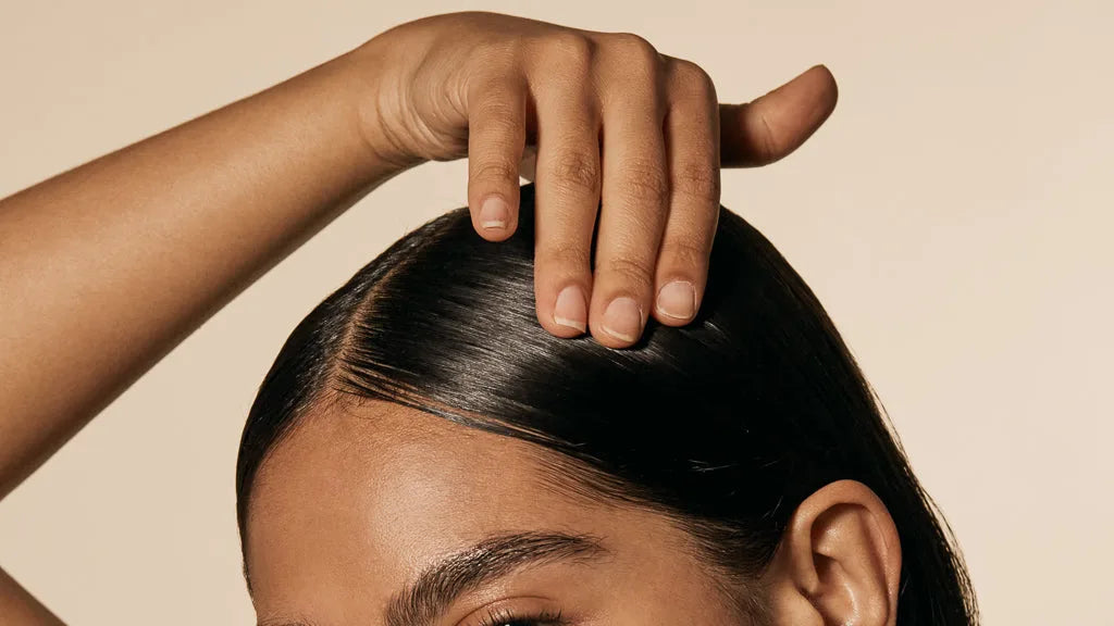 Glossy dark hair styled with a smooth center part, hand resting near the sleek crown.