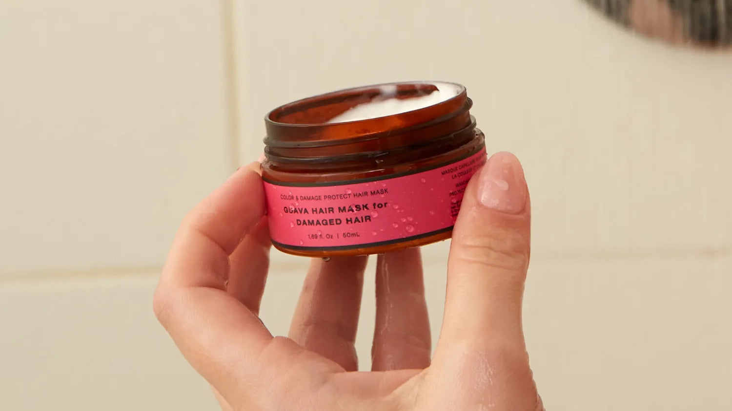 Hand holding an open travel-size Guava hair mask for damaged hair, 50mL jar.