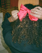 Pink hair bow being tied onto curly hair by a person wearing a black top.