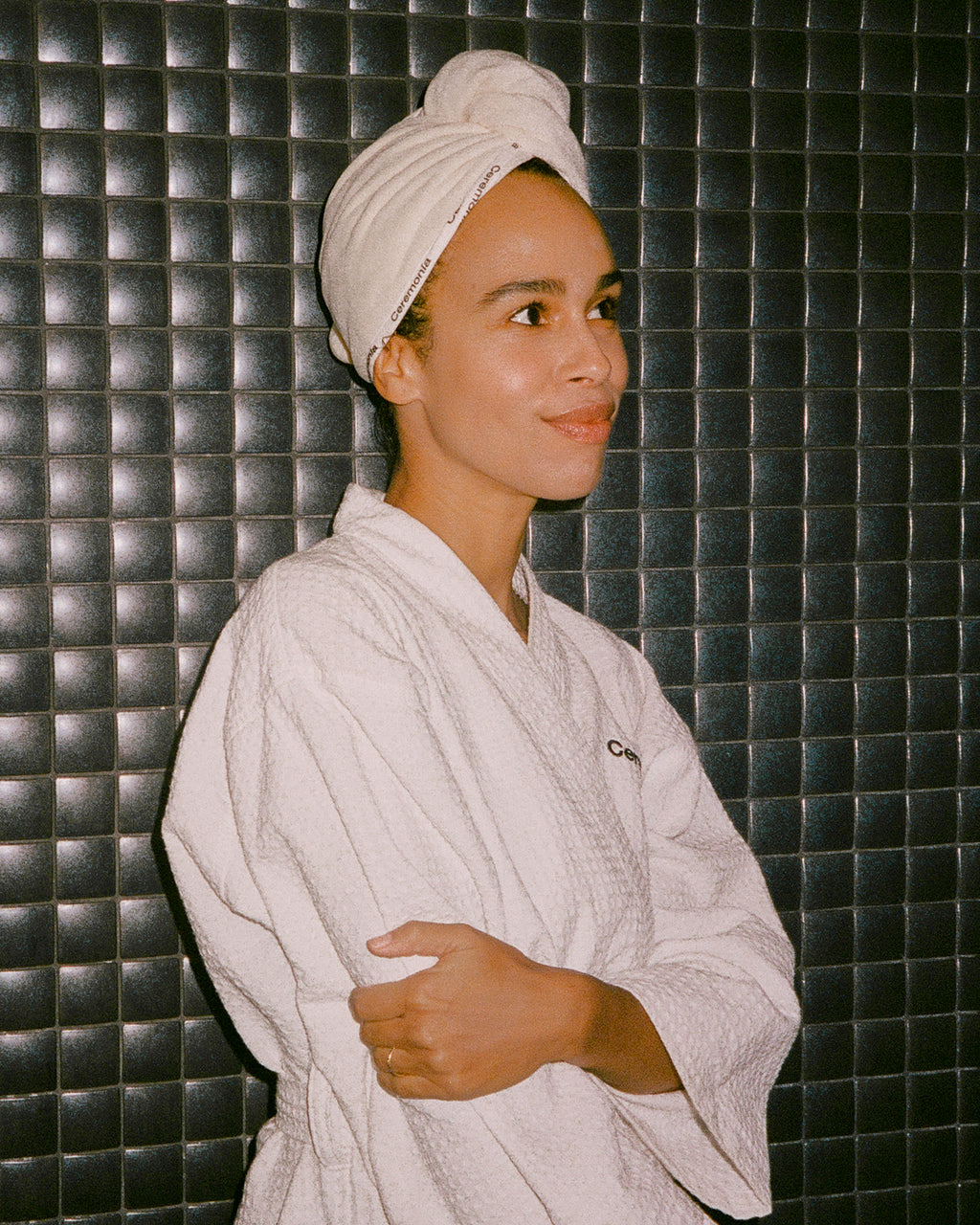Hair towel wrapped around head with Ceremonia branding, worn with a matching white robe against a tiled wall background.