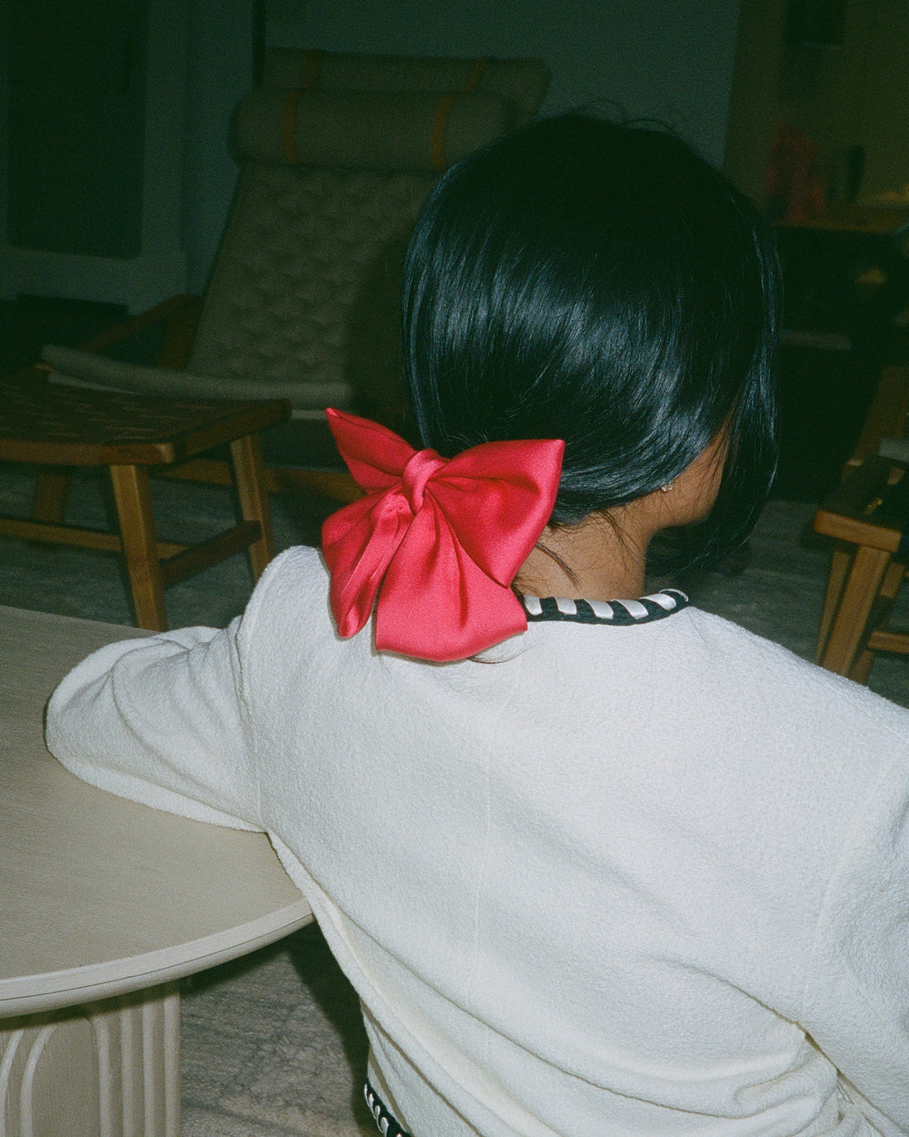 Back view of a red satin bow hair clip fastened in sleek dark hair above a cream sweater.