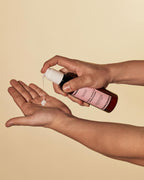 Hair repair cream being dispensed from a Ceremonia Guava Leave-In Conditioner bottle into an open palm against a beige background.