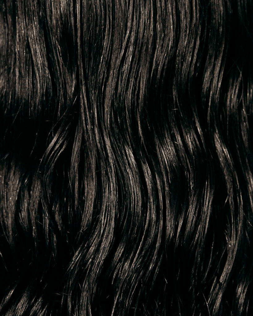 Close-up of glossy, frizz-free dark wavy hair showing shine after Oil Mist con Aloe Vera.