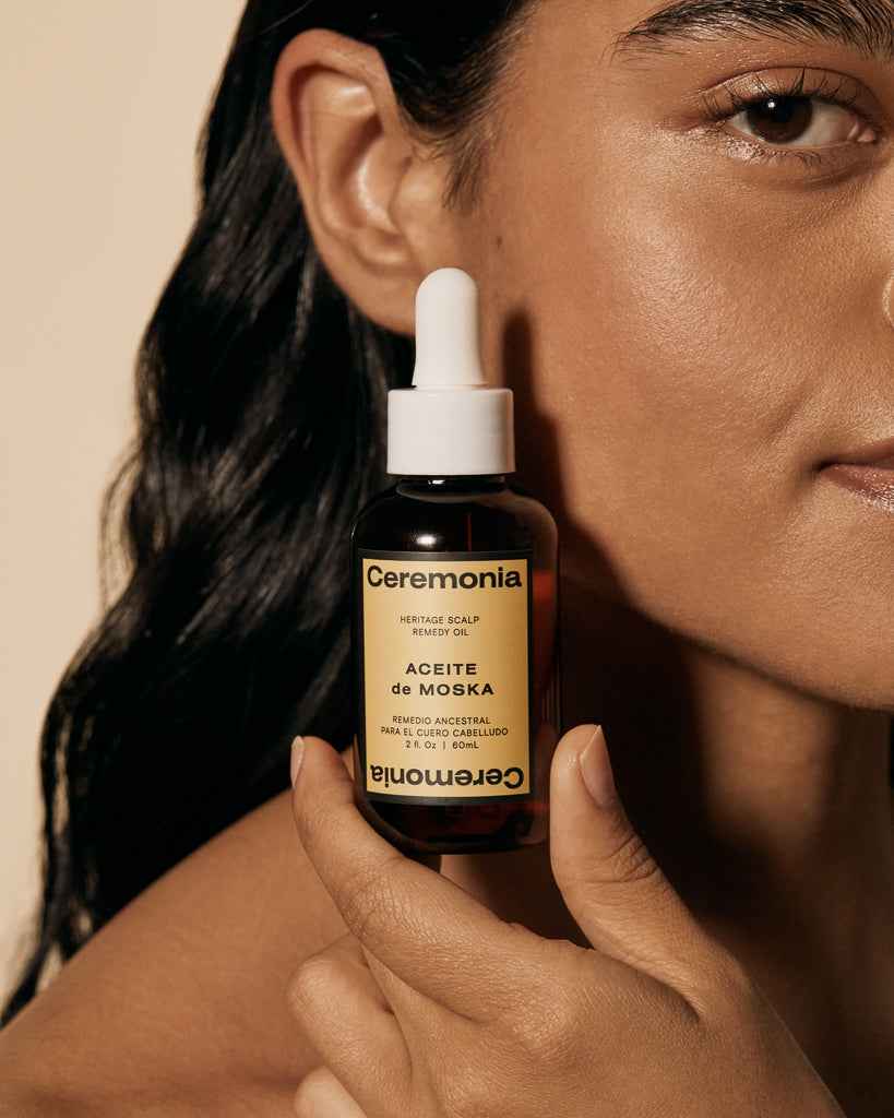 Scalp oil held close to the face, featuring Ceremonia Aceite de Moska for nourishing and treating the scalp.