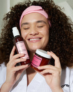 Guava hair mask held by a smiling woman with curly hair, wearing a pink headband and white robe.