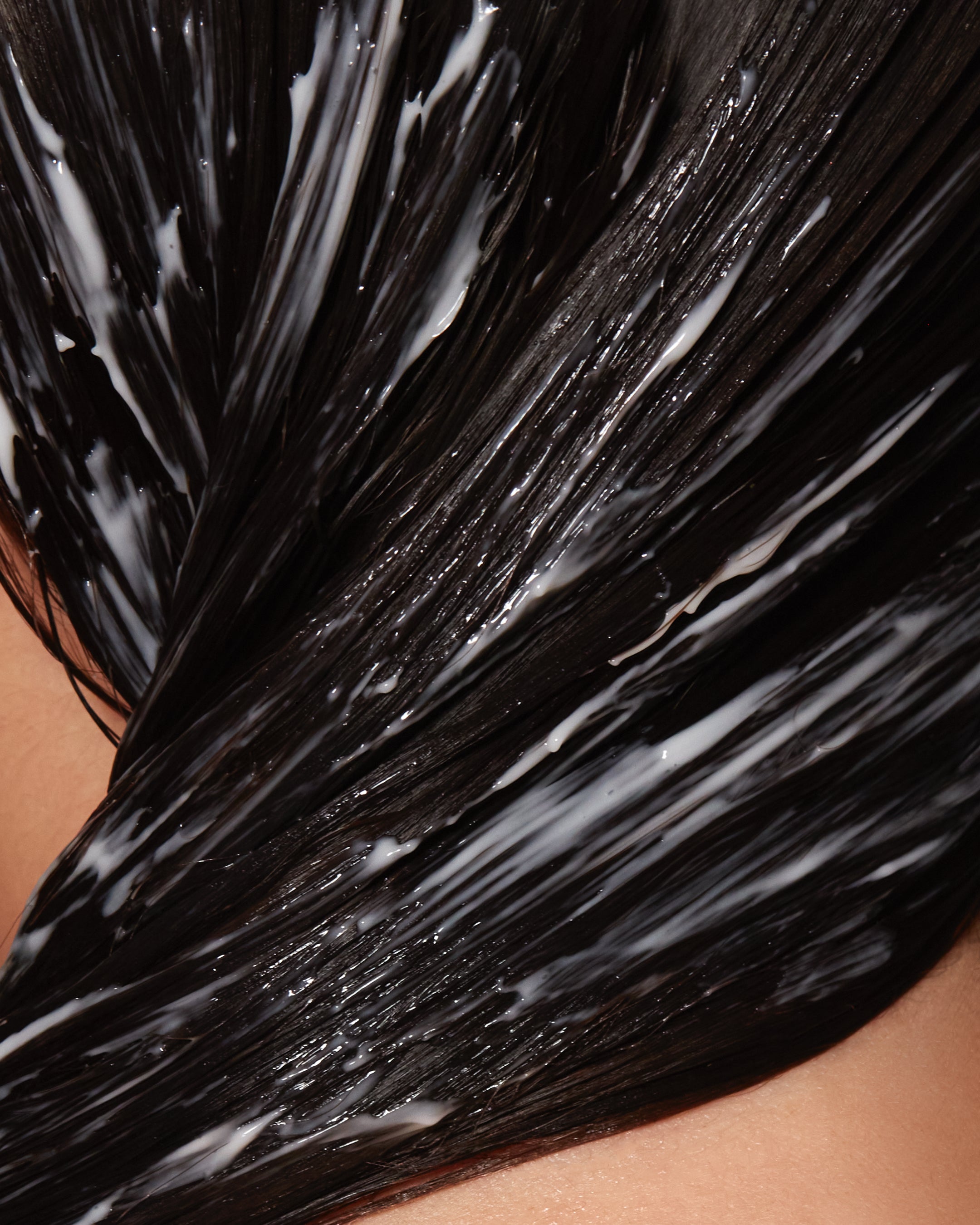 Close-up of wet dark hair coated in creamy white guava hair mask for damage repair.