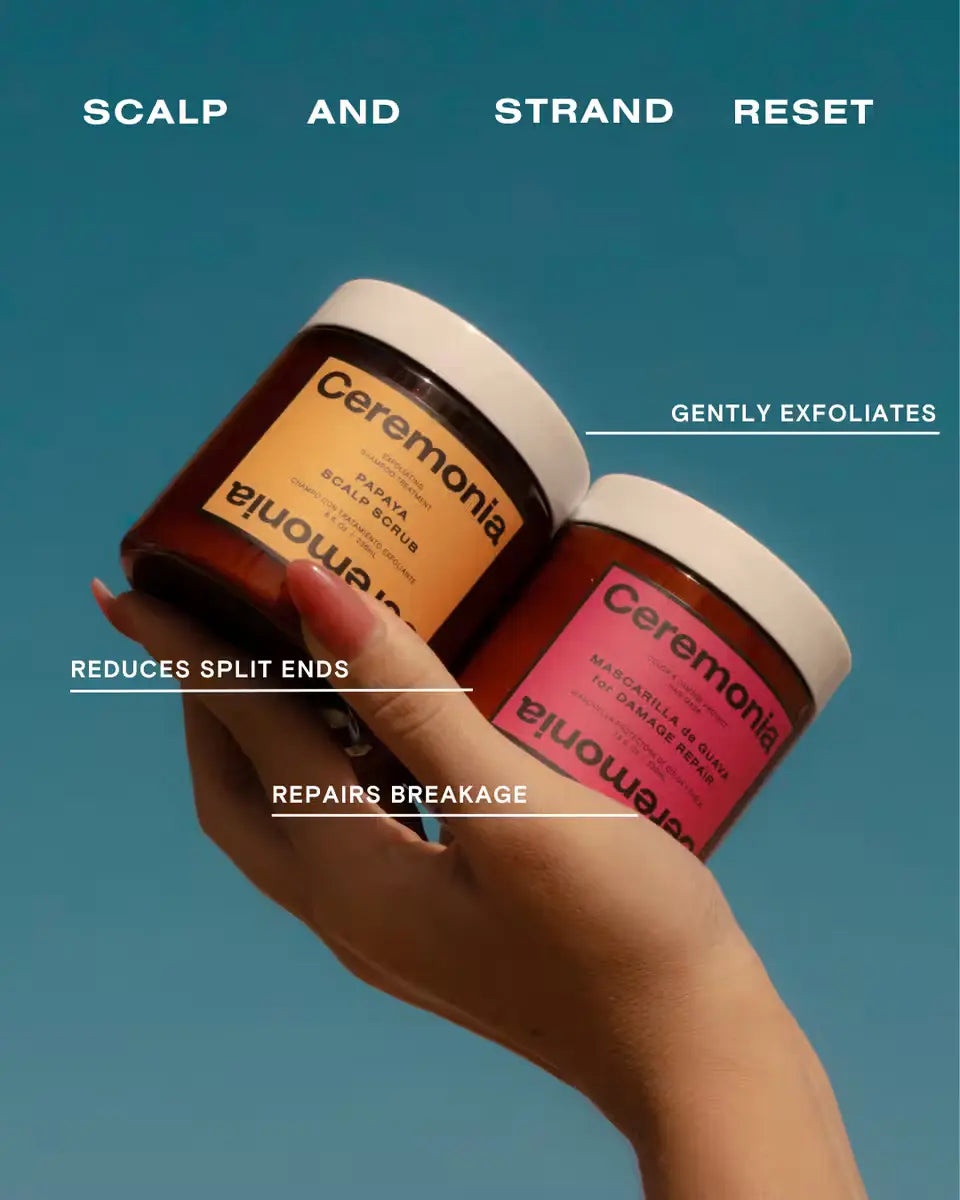 Papaya shampoo and guava hair mask jars held in hand against blue sky for scalp exfoliation and hair repair.