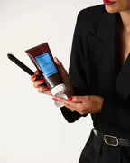 Hair styling gel being dispensed into a woman's hand from a Ceremonia-branded tube with a sleek black outfit.