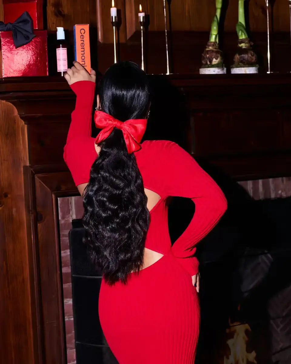 Long wavy natural curls held with a red satin bow clip, reaching for Ceremonia products by candlelight.