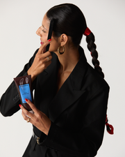 Hair styling gel being applied by a woman with a sleek braided ponytail and bold red accessories.