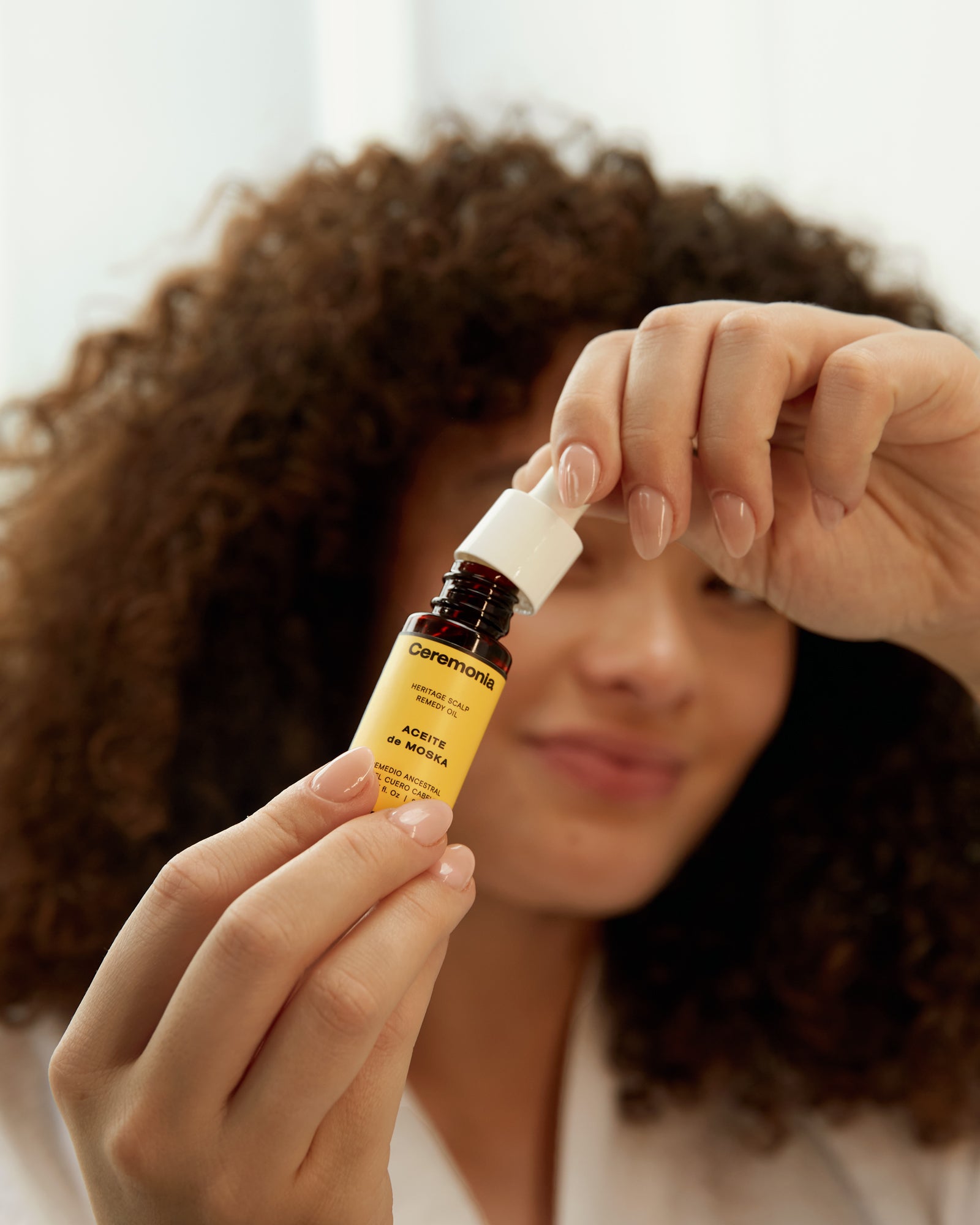 Scalp oil from Ceremonia held by a woman preparing to apply the heritage remedy to her curly hair.