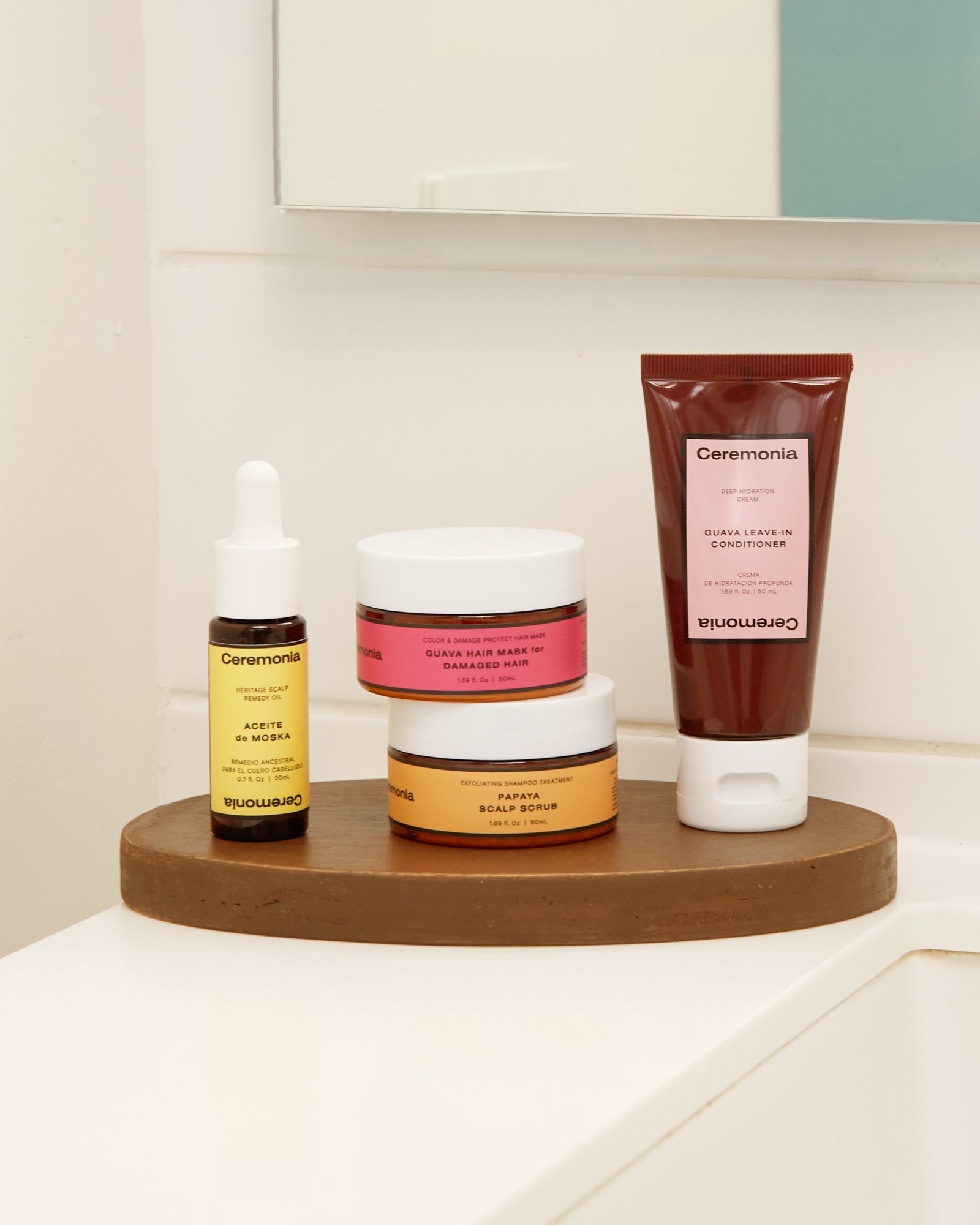 Guava hair mask for damaged hair displayed with Ceremonia's scalp oil, papaya scalp scrub, and leave-in conditioner on a bathroom shelf.