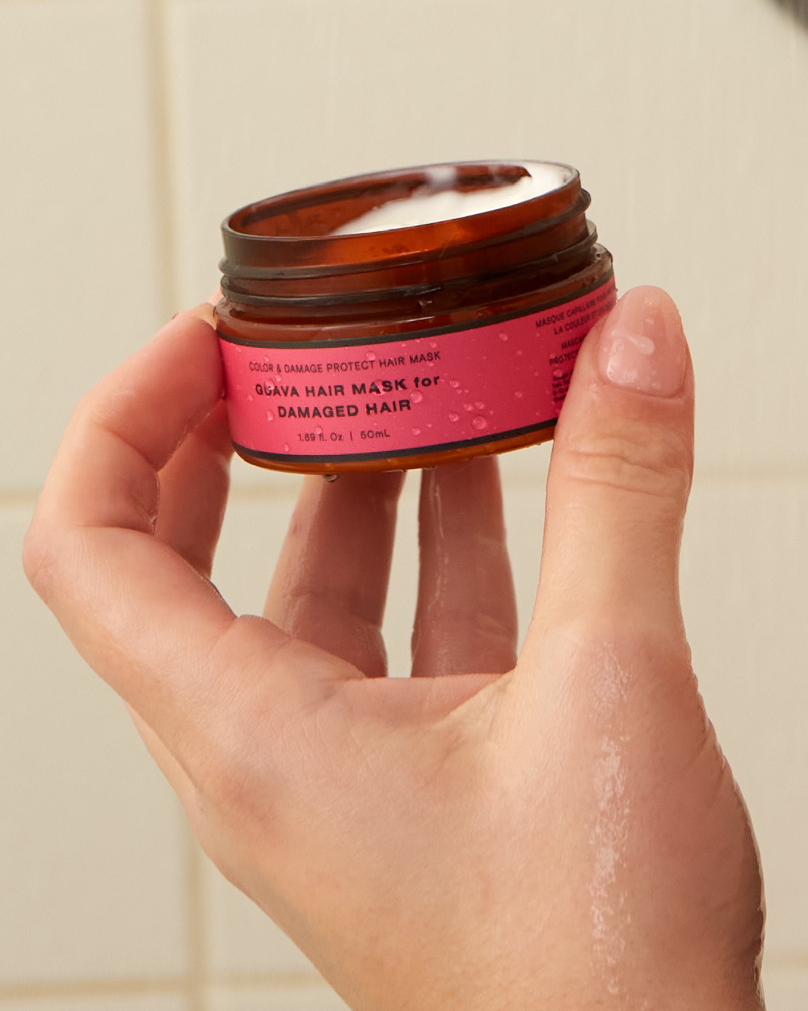 Guava hair mask for damaged hair held in a hand, showing creamy texture and pink product label.