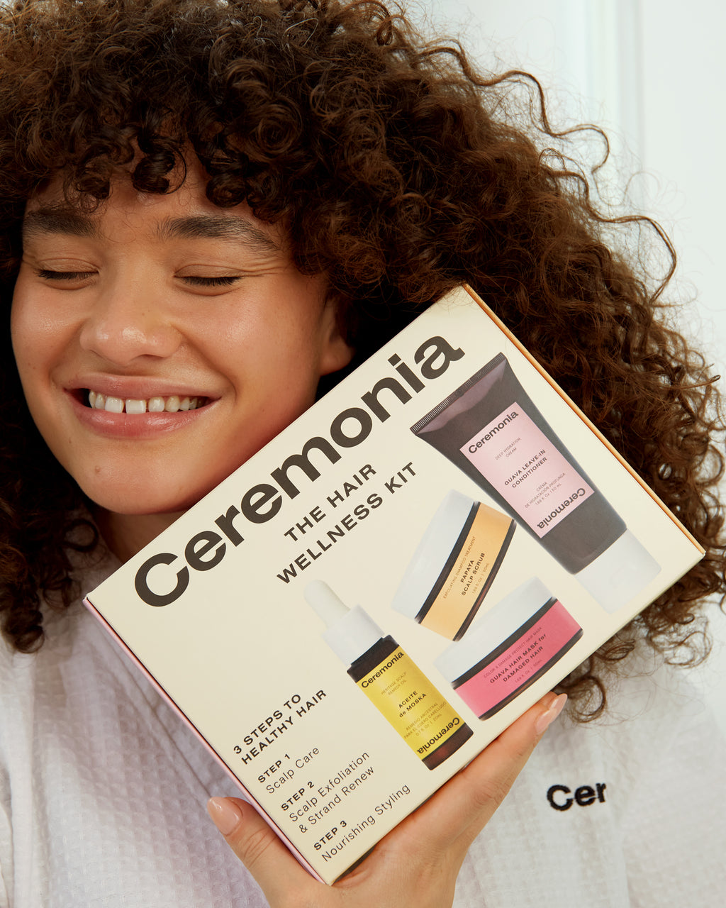 Guava leave-in conditioner included in Ceremonia’s Hair Wellness Kit held by a smiling woman with curly hair.