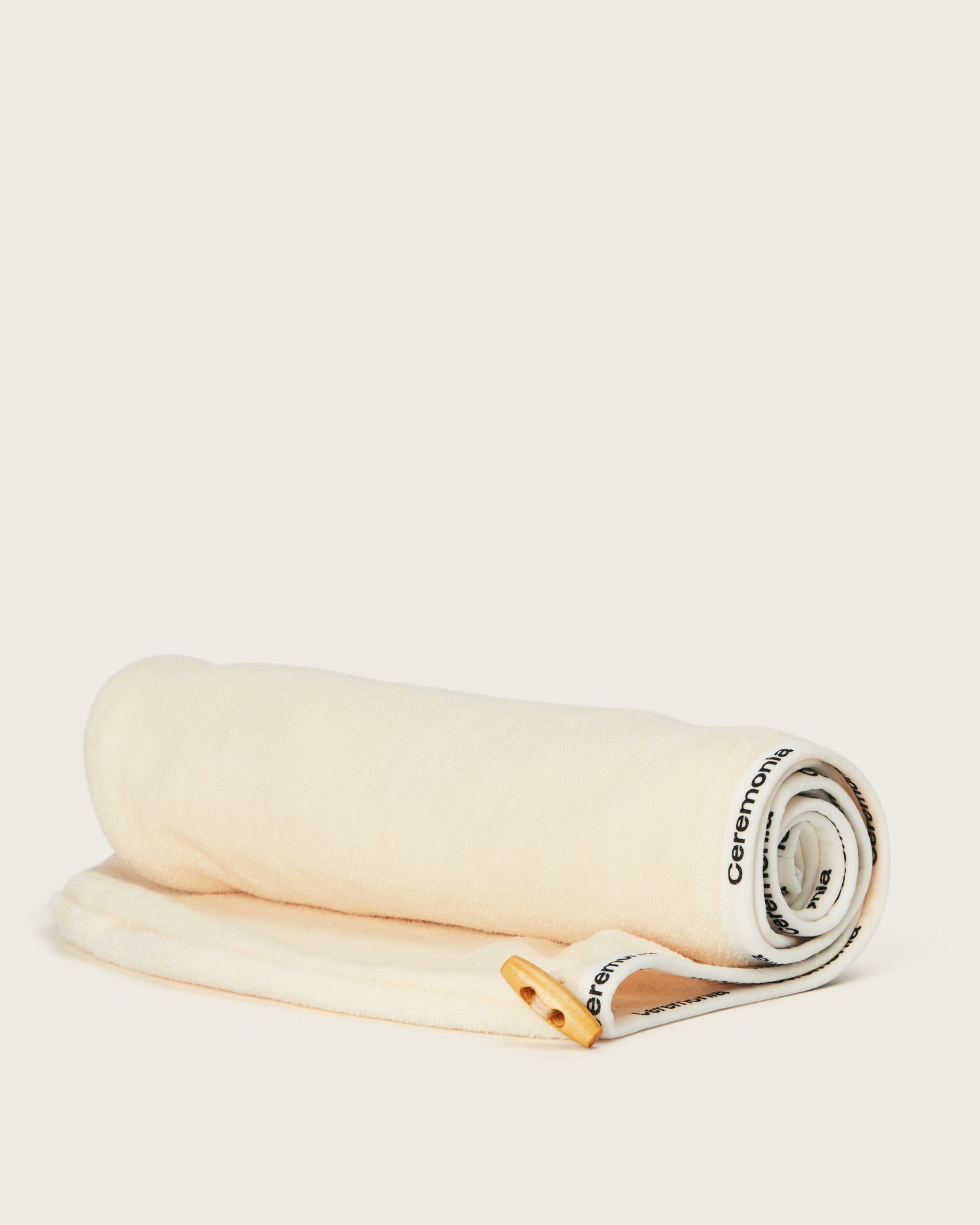 Hair towel in soft beige fabric with Ceremonia branding and wooden button detail, displayed unboxed.