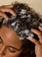 Exfoliating scalp mask being massaged into wet curly hair, creating a rich lather for deep scalp cleansing and refreshment.