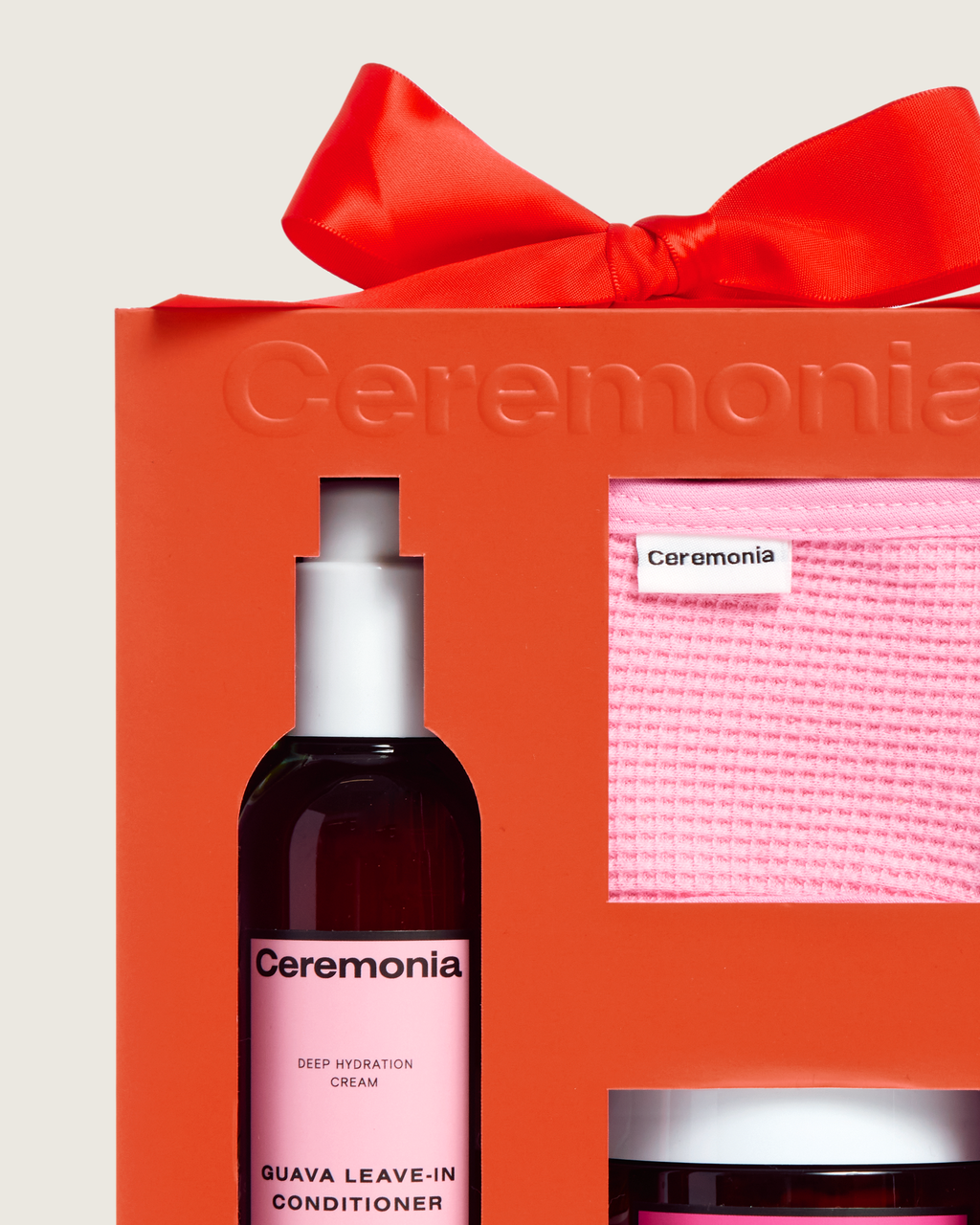 Guava leave-in conditioner displayed in a bright orange Ceremonia gift box with a red bow and pink towel headband.