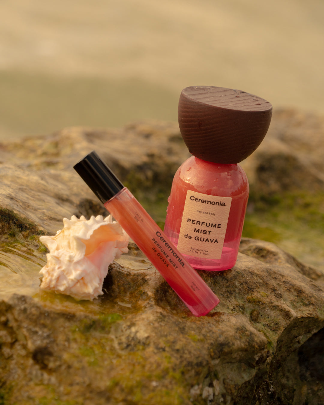 Guava perfume mist bottles placed on wet seaside rocks with a seashell, capturing a tropical and refreshing beach vibe.