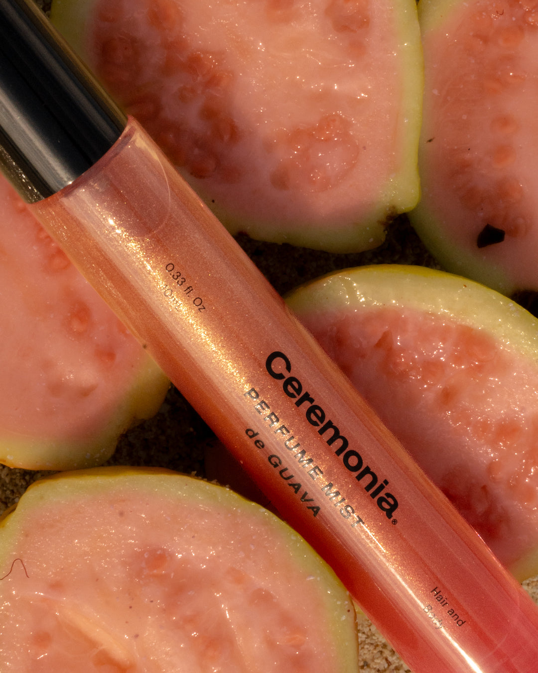 Guava perfume mist bottle with shimmer finish placed on freshly sliced pink guavas for a tropical aesthetic.