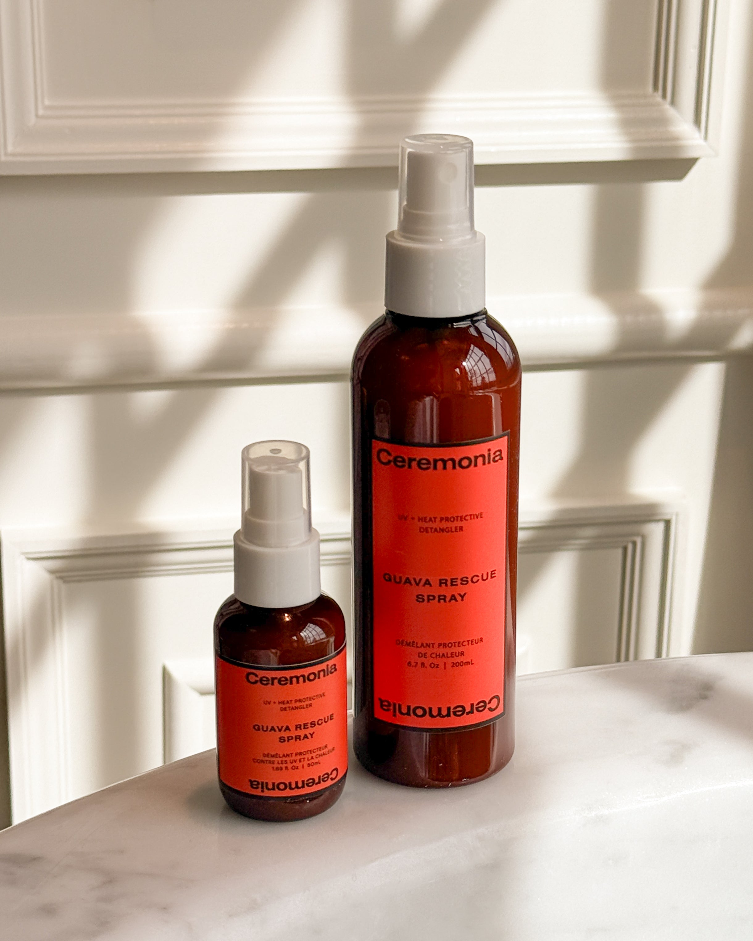 Hair detangler spray duo labeled Guava Rescue Spray placed on a marble counter with soft natural light and shadows.