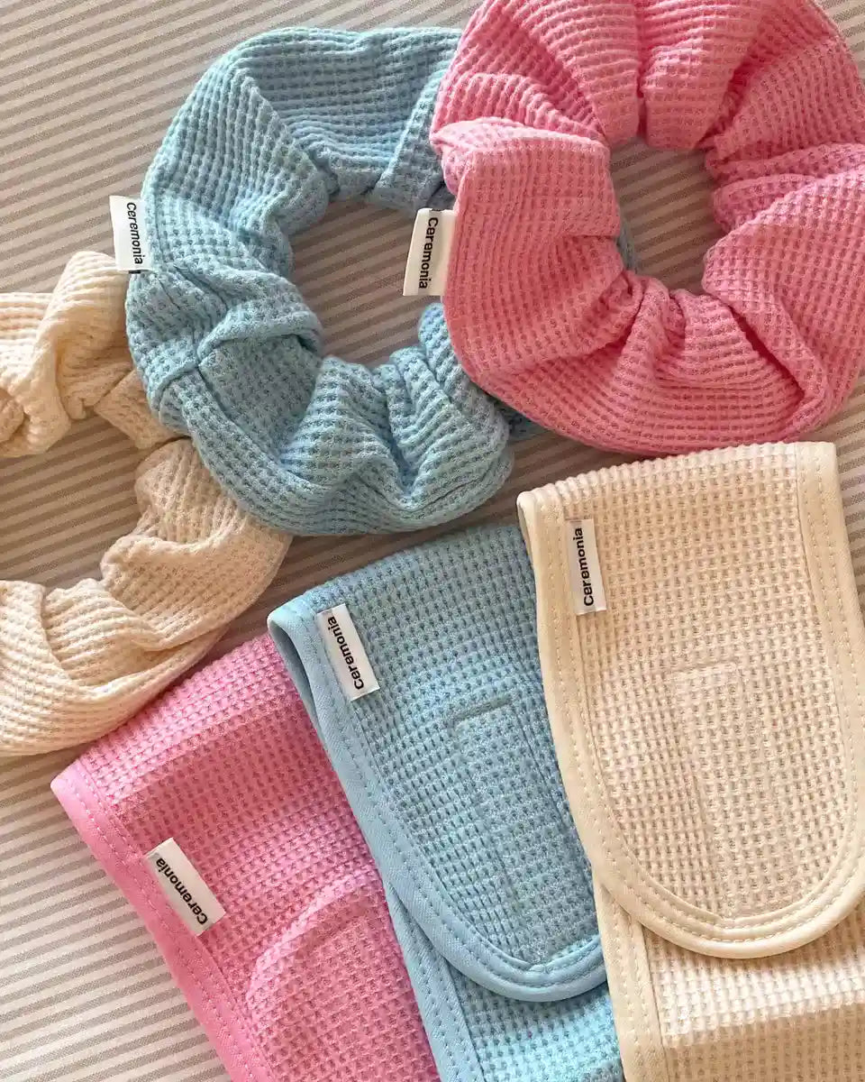 Pink scrunchie made of waffle-textured fabric alongside pastel blue and cream accessories from Ceremonia brand.