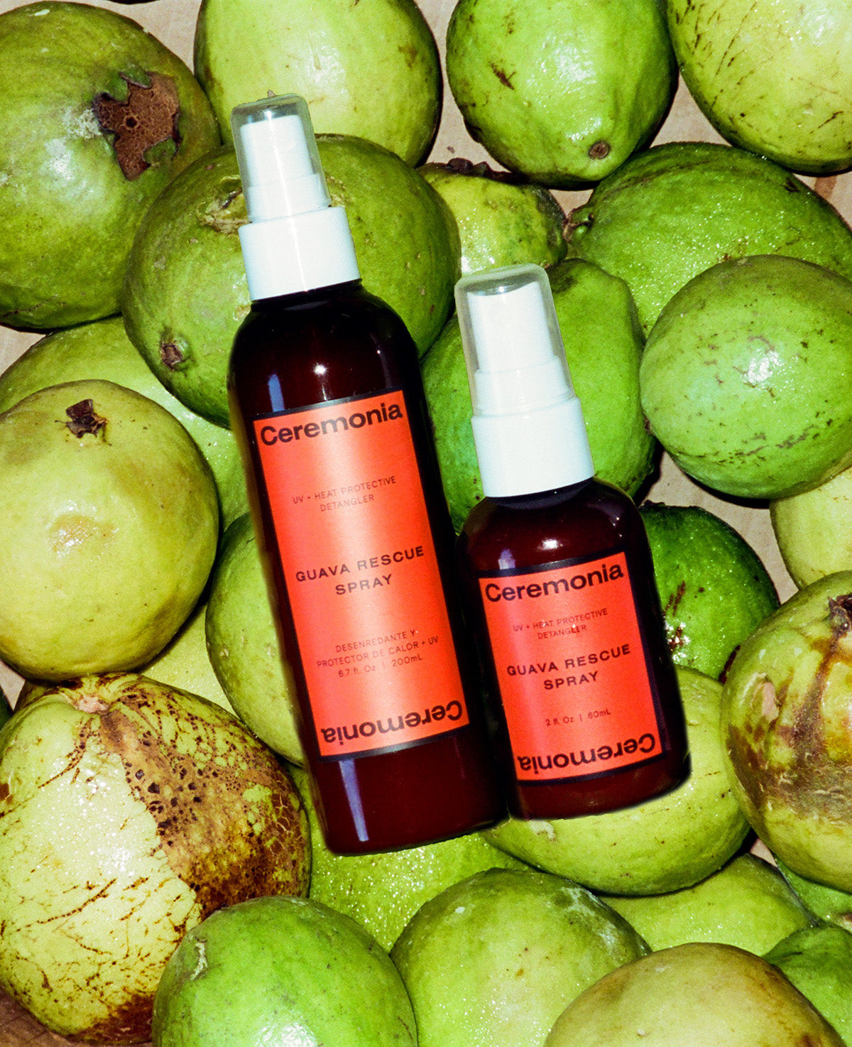 Hair detangler spray bottles labeled Guava Rescue Spray placed on fresh green guavas for a vibrant tropical display.