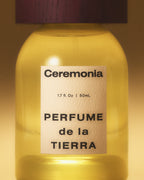 Perfume mist de la Tierra in a yellow glass bottle with a wooden cap, shown in warm golden lighting.