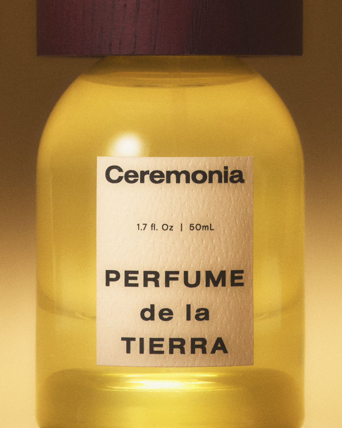 Perfume mist de la Tierra in a yellow glass bottle with a wooden cap, shown in warm golden lighting.