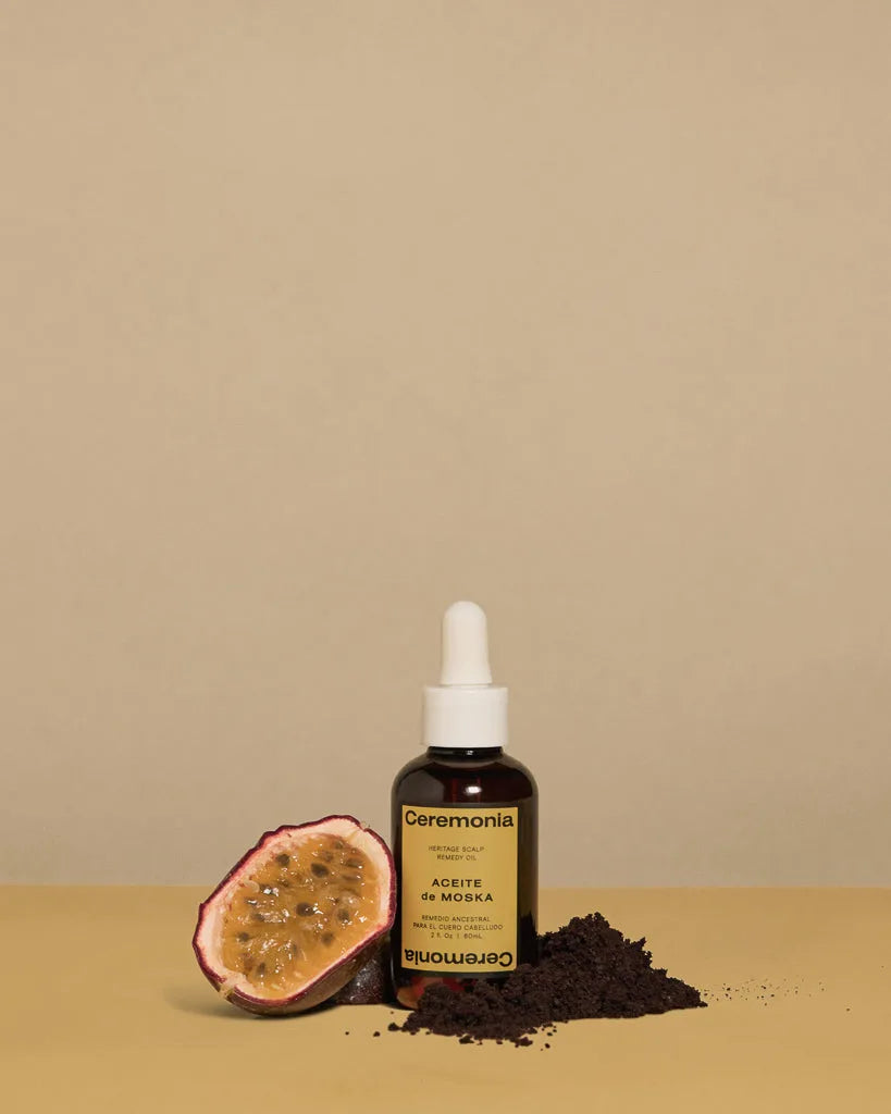Ceremonia Aceite de Moska scalp oil bottle beside halved passionfruit and açai powder.