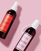Ceremonia Guava Rescue Spray and Guava Leave-in Conditioner bottles with a dollop of cream on a pink background.