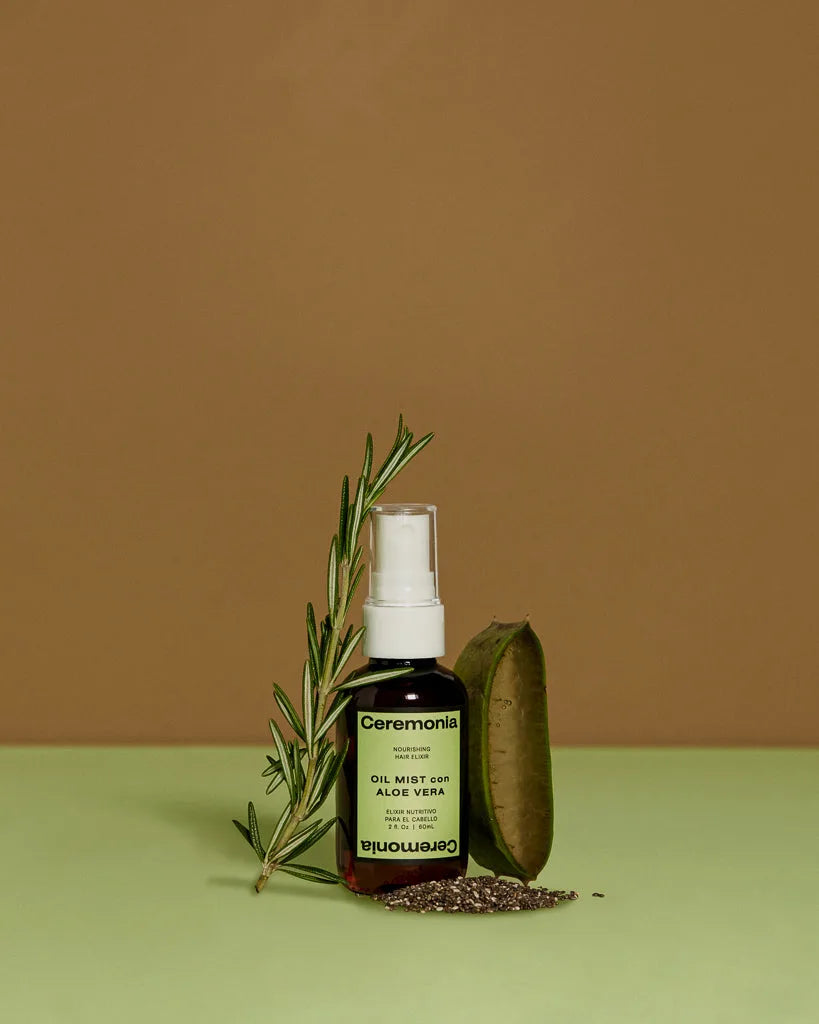 Ceremonia Oil Mist con Aloe Vera bottle beside fresh rosemary, aloe leaf, and chia seeds.