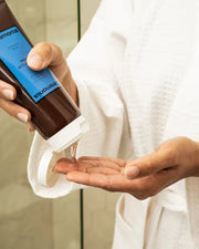 Hair styling gel being squeezed into a hand from a Ceremonia tube by a person wearing a white bathrobe.