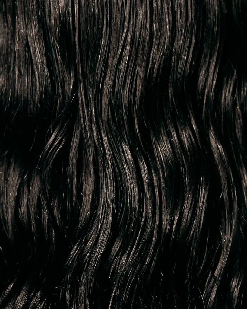 Close-up of glossy, frizz-free dark wavy hair showing shine after Oil Mist con Aloe Vera.