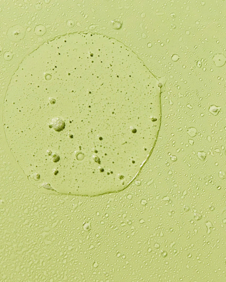 Close-up texture swatch of green aloe vera hair oil mist with fine droplets.