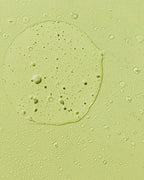 Close-up texture swatch of green aloe vera hair oil mist with fine droplets.