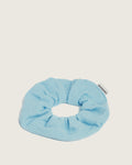 Blue scrunchie made of textured fabric with a Ceremonia tag on a neutral background.