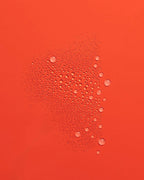 Fine mist of Guava Rescue Spray droplets scattered across a vivid red-orange surface.