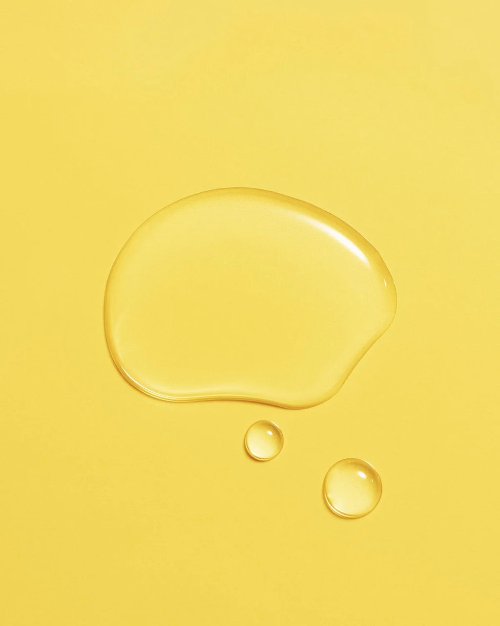 Golden droplet of Aceite de Moska scalp oil pooled on a pale yellow surface.