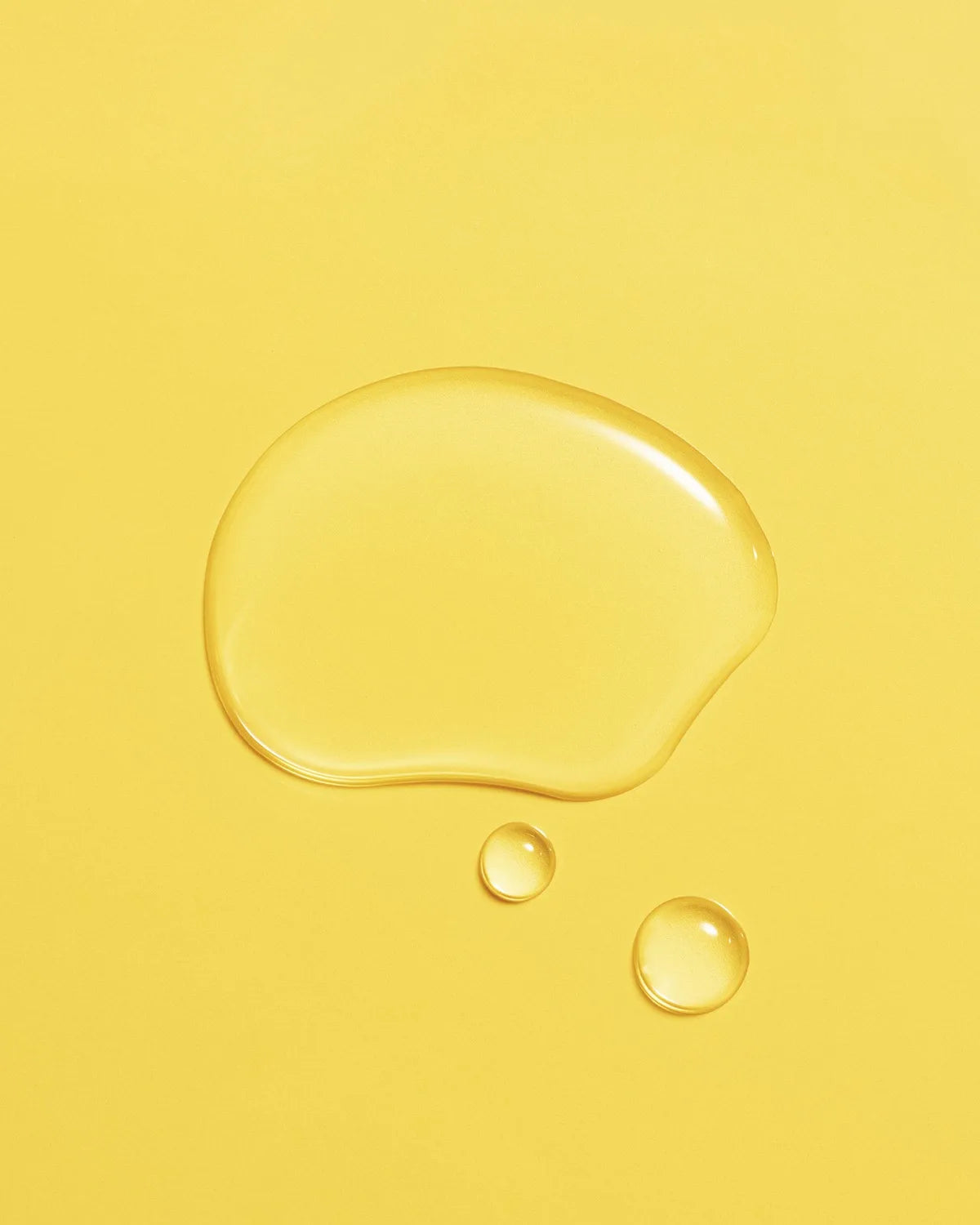 Golden droplet of Aceite de Moska scalp oil pooled on a pale yellow surface.