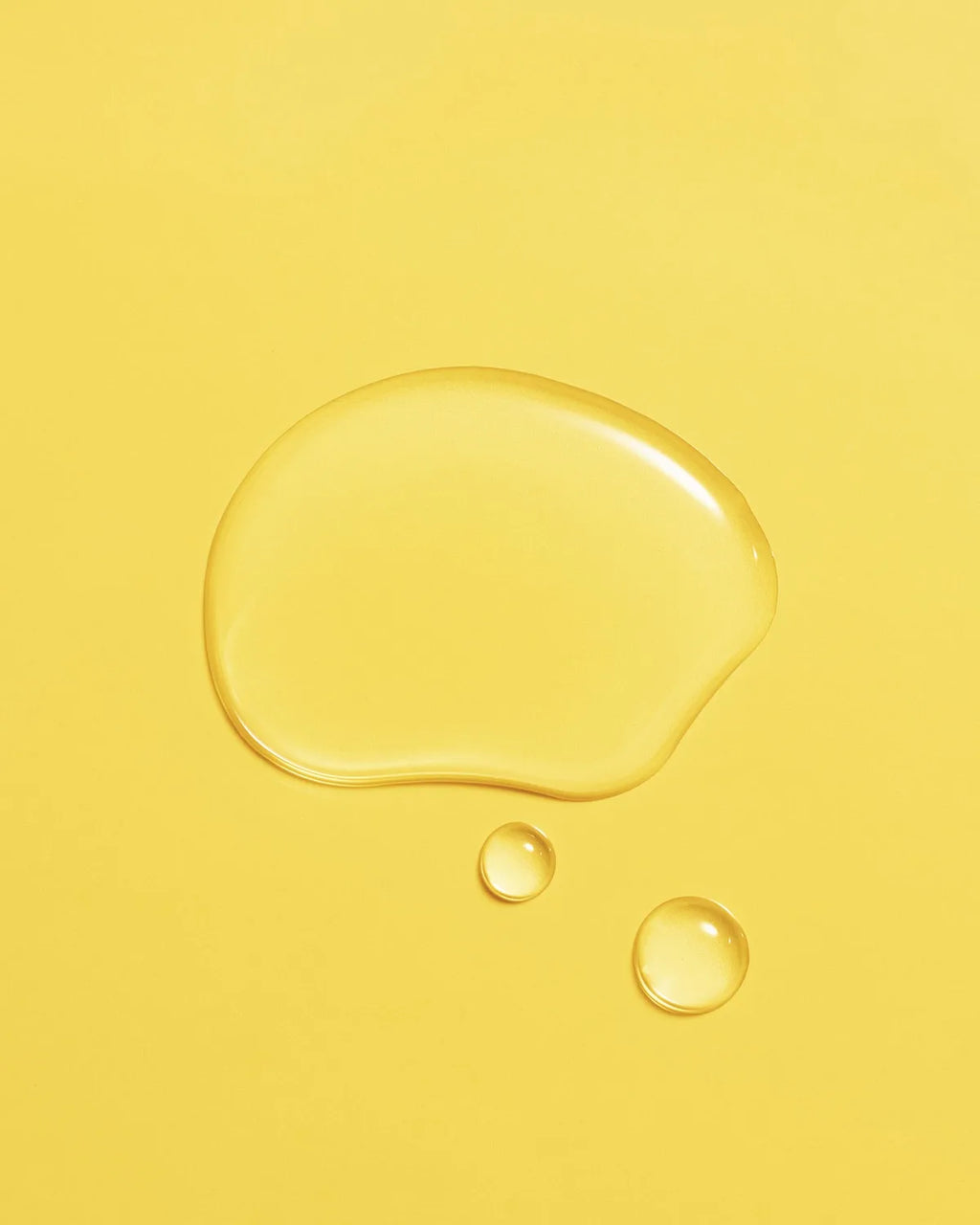 Golden droplet of Aceite de Moska scalp oil pooled on a yellow surface.