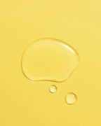 Golden droplet of Aceite de Moska scalp oil pooled on a yellow surface.