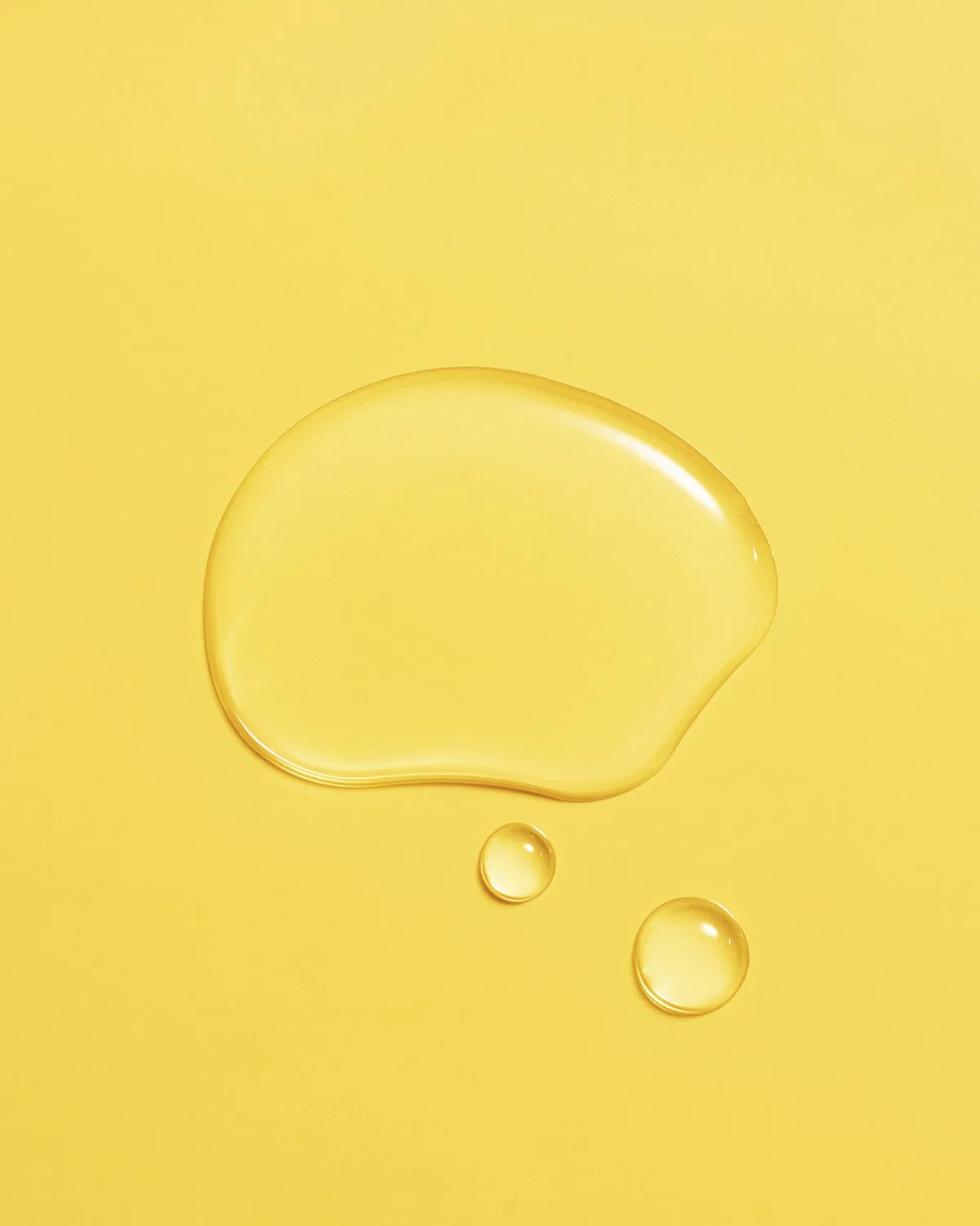 Golden droplet of Aceite de Moska scalp oil pooled on a yellow surface.
