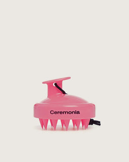 Guava pink Ceremonia scalp massager with silicone bristles and black wrist strap.