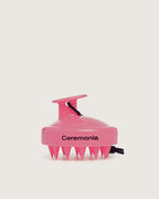 Guava pink Ceremonia scalp massager with silicone bristles and black wrist strap.